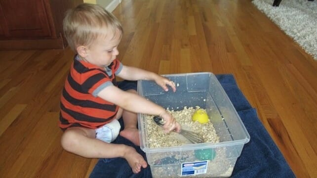 Boy playing in a sensory tub with oats and water