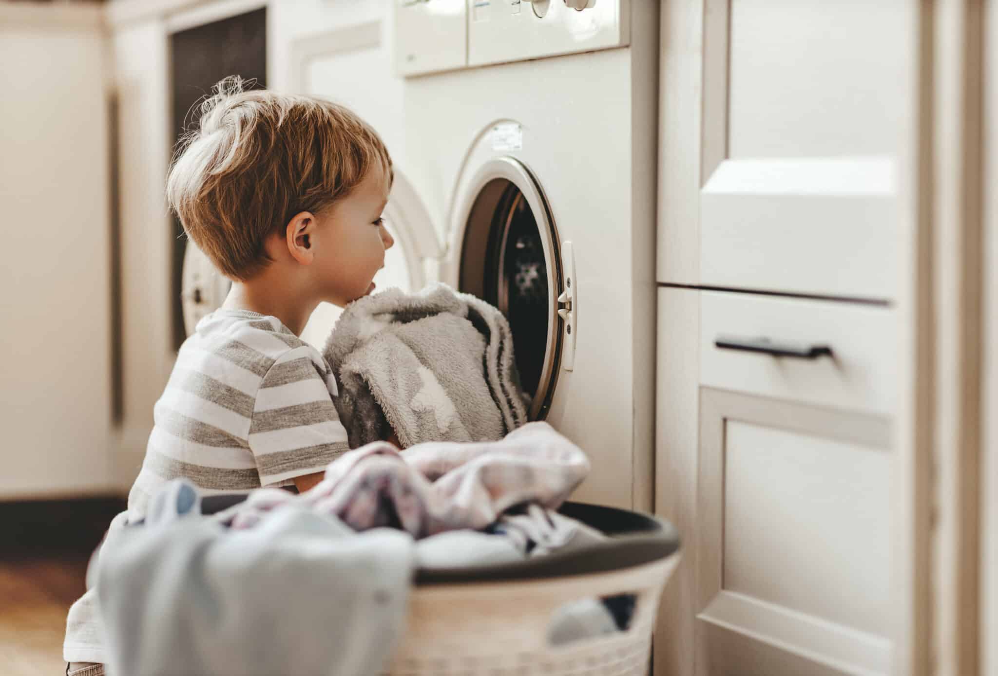 happy little funny householder child boy in laundry with washing machine