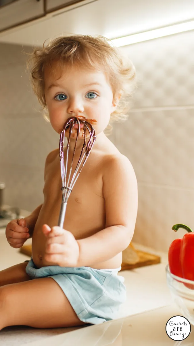 a child tasting a whisk covered in batter