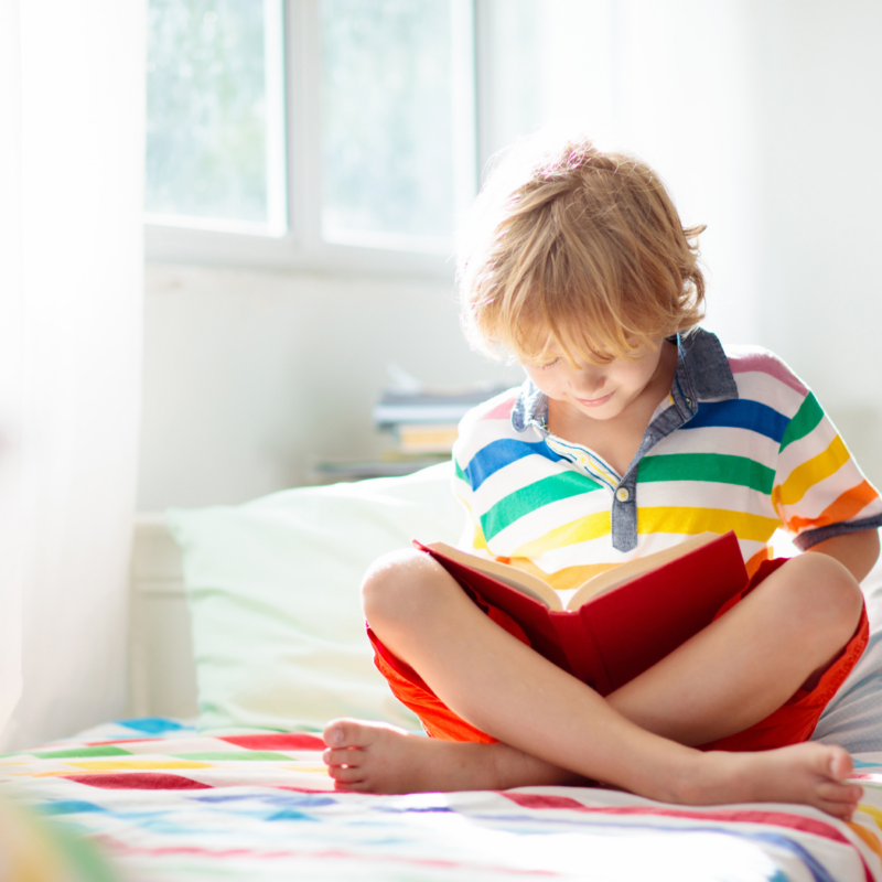 A young boy reading a book in bed