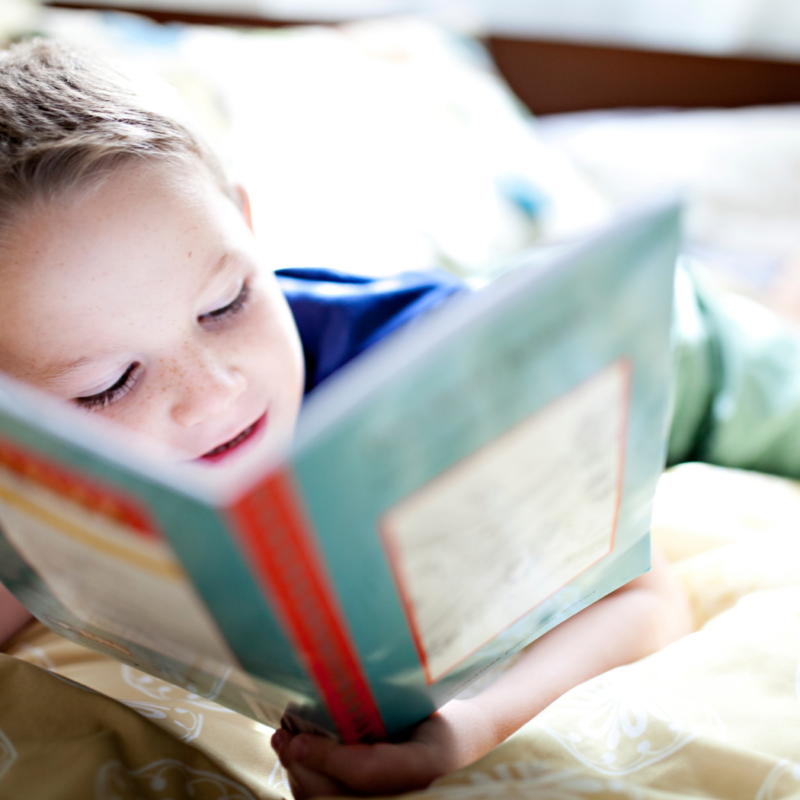 A young boy smiling reading a book