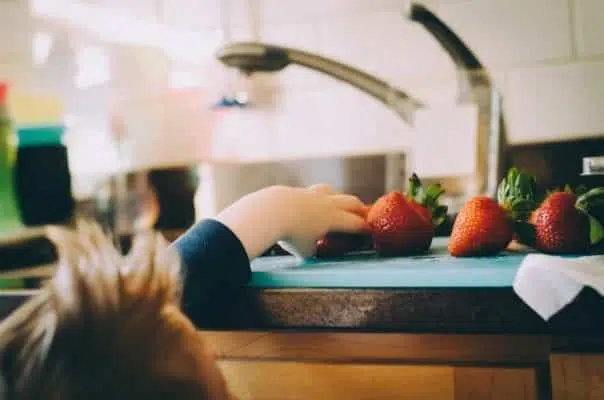 A child reaching for a strawberry.