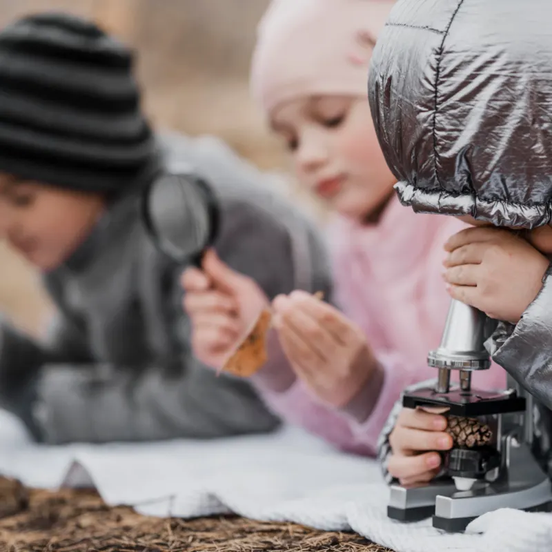 children learning outside with a microscope and magnifying glass