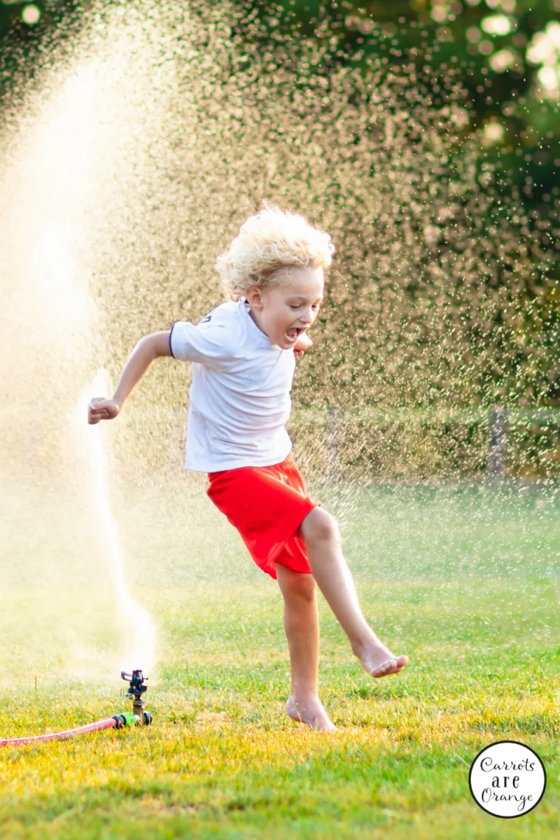 a young boy jumping through a sprinkler