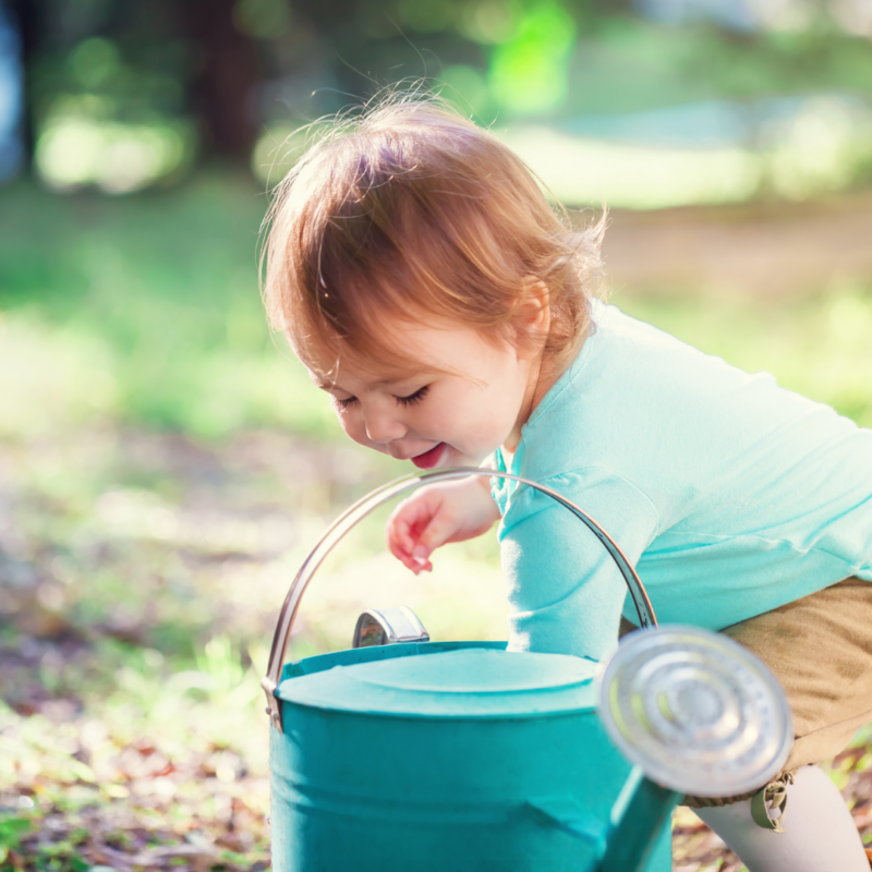 a toddler playing outside with a watering can