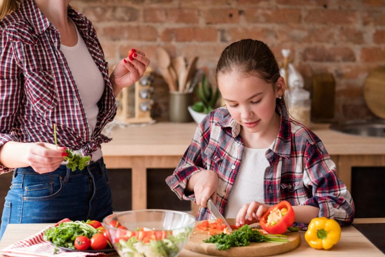 little cook. adolescent girl cutting vegetables and preparing dinner from fresh organic food ingredients. healthy eating and wholesome nutrition concept.
