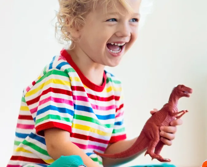 A young boy smiling playing with a dinosaur