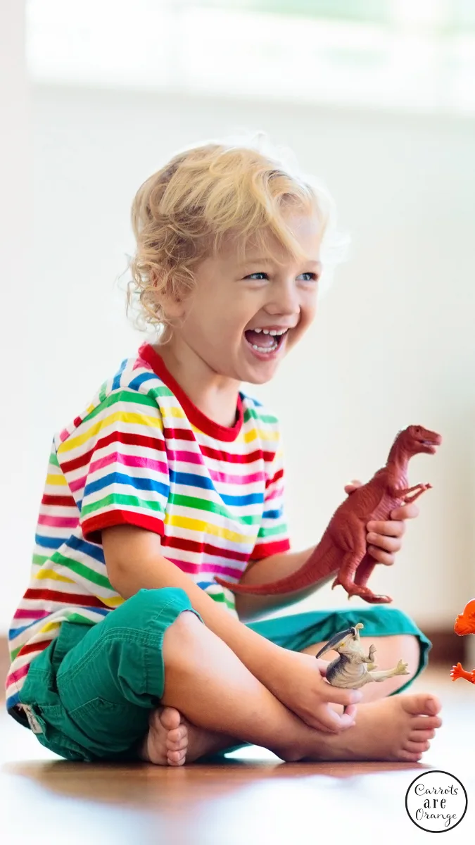 A young boy smiling playing with a dinosaur