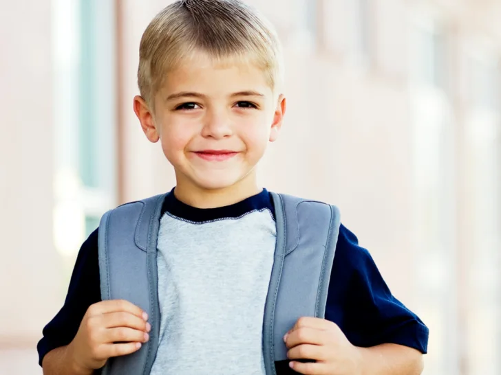 A young boy smiling with a backpack on