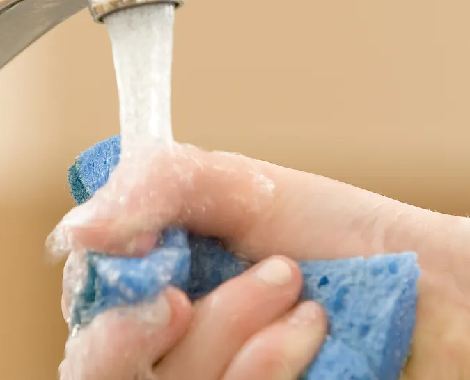 A person squeezing a sponge under a faucet