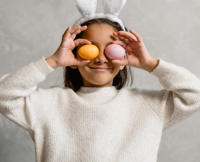 A girl wearing bunny ears and putting two eggs in front of her eyes