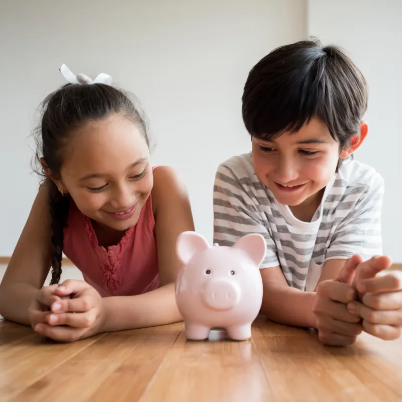 Smiling girl and boy staring at a piggy bank