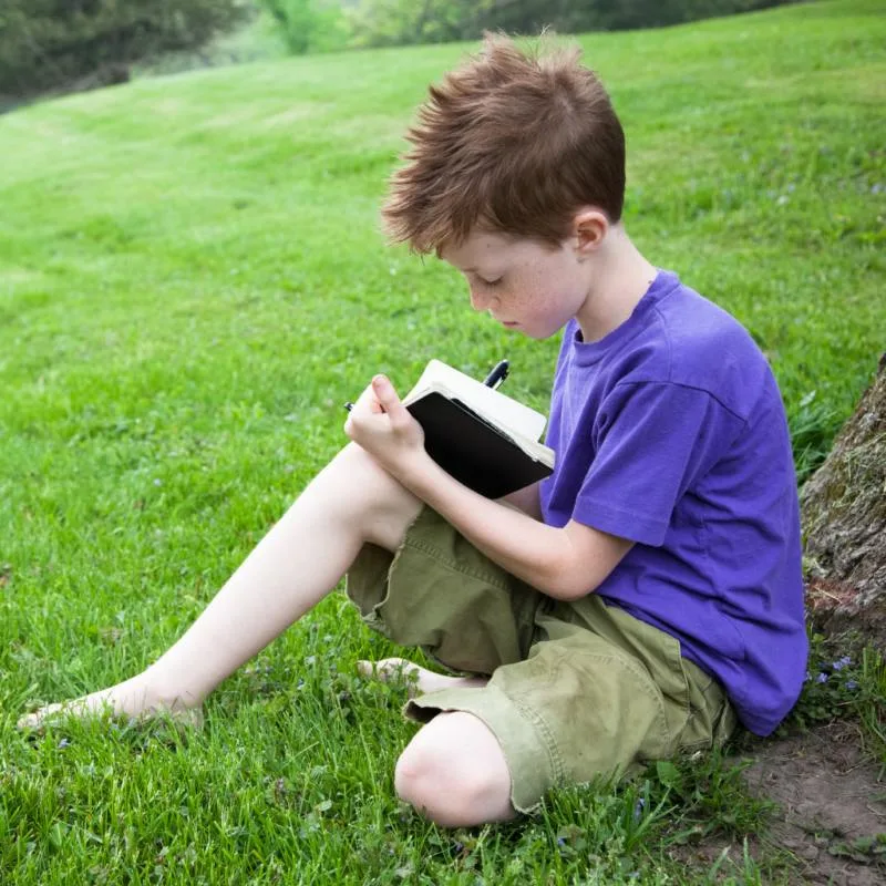 a boy sitting outside writing in a journal