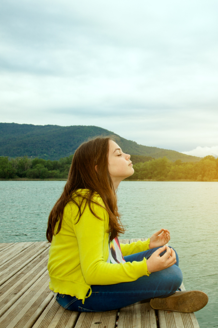 a young girl meditating on a dock on a lake