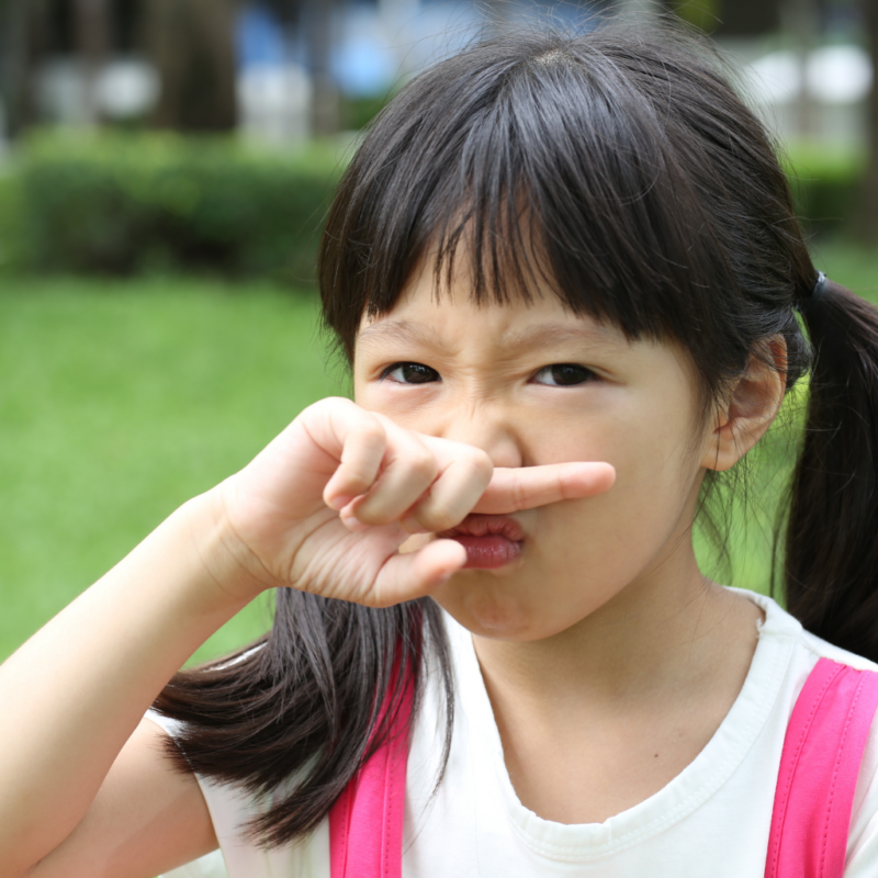 young asian girl with finger at her nose not liking a smell